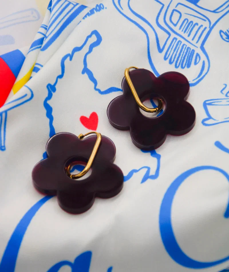 Pendientes flor morados con aro dorado sobre tela estampada, joyería artesanal inspirada en Colombia