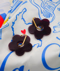 Pendientes flor morados con aro dorado sobre tela estampada, joyería artesanal inspirada en Colombia