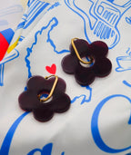 Pendientes flor morados con aro dorado sobre tela estampada, joyería artesanal inspirada en Colombia
