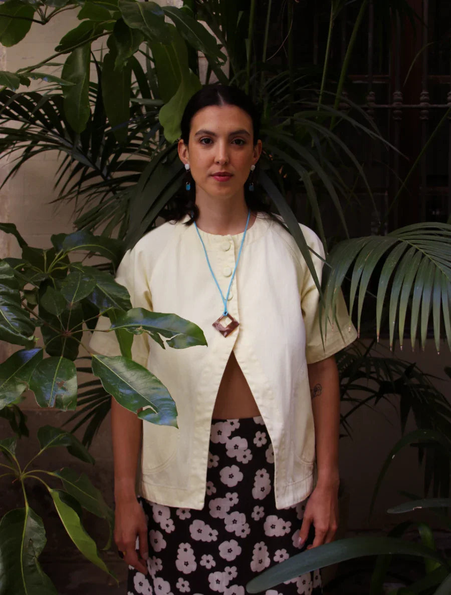 Mujer con collar artesanal hecho a mano en resina UV con colgante geométrico en forma de rombo de color café, con hilo azul y aretes azules. Joyería inspirada en la cultura colombiana.