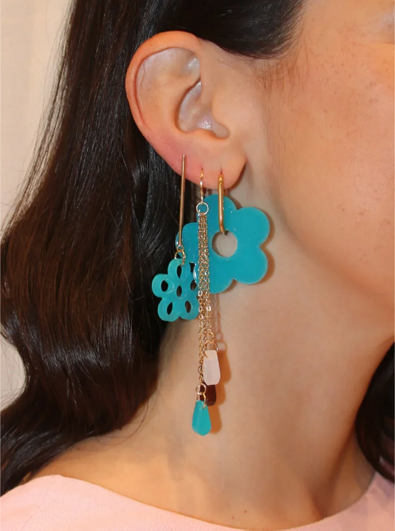 Pendientes artesanales hechos a mano en resina UV, color azul cielo con forma de flor y silueta de flor, combinados con pendientes de cadena fina en acero inoxidable dorado, con gotas de colores. Joyería artesanal inspirada en Colombia