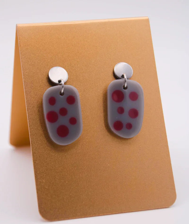 Pendientes artesanales con diseño de puntos rojos sobre fondo gris, inspirados en la cultura colombiana